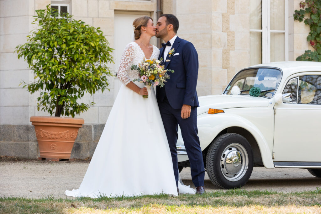 deux mariés s'embrassant devant leur voiture balais prise lors d'un mariage en vendée par la photographe